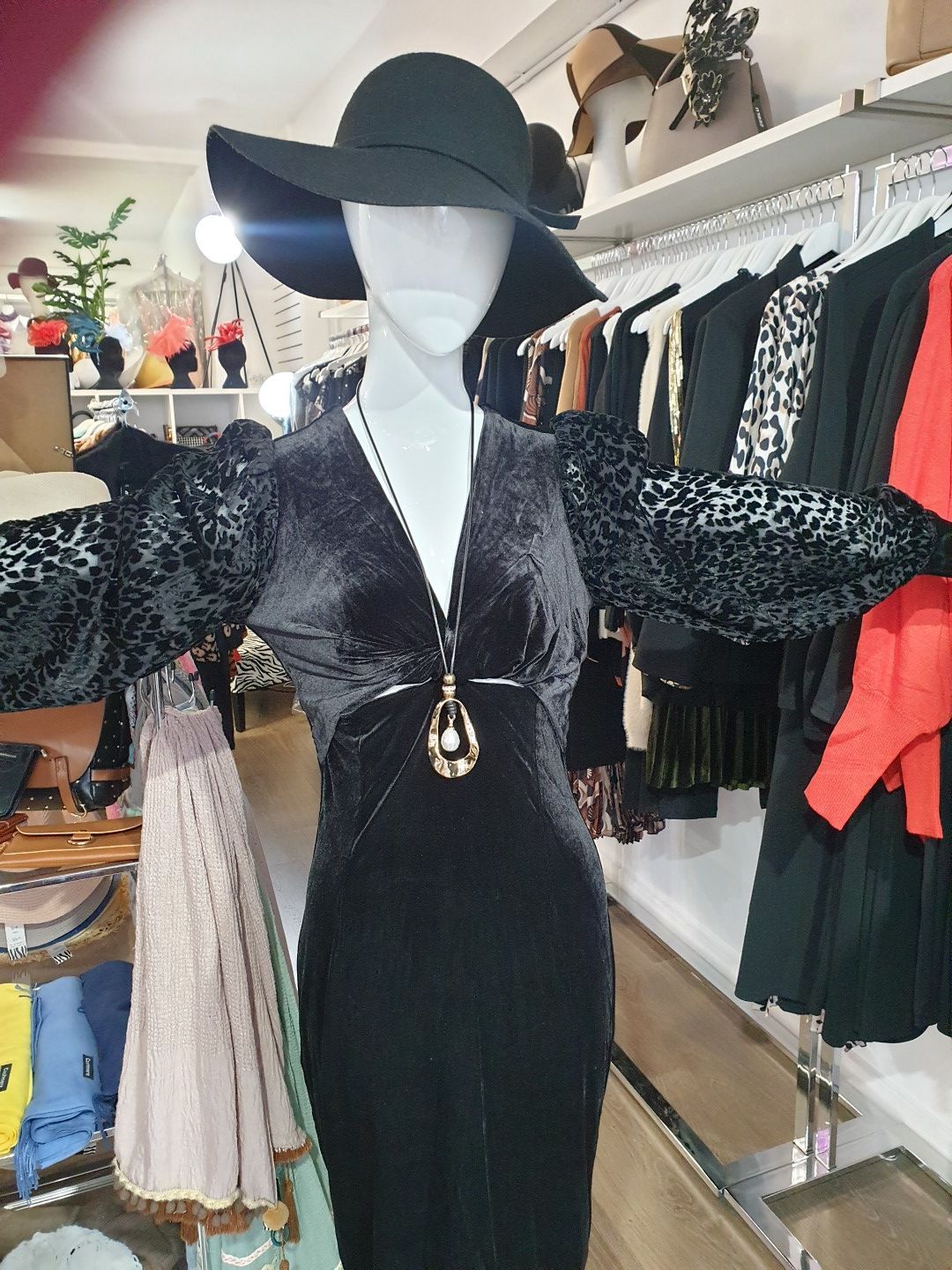 Mannequin in black velvet dress with large hat, leopard print sleeves, standing in a clothing store.