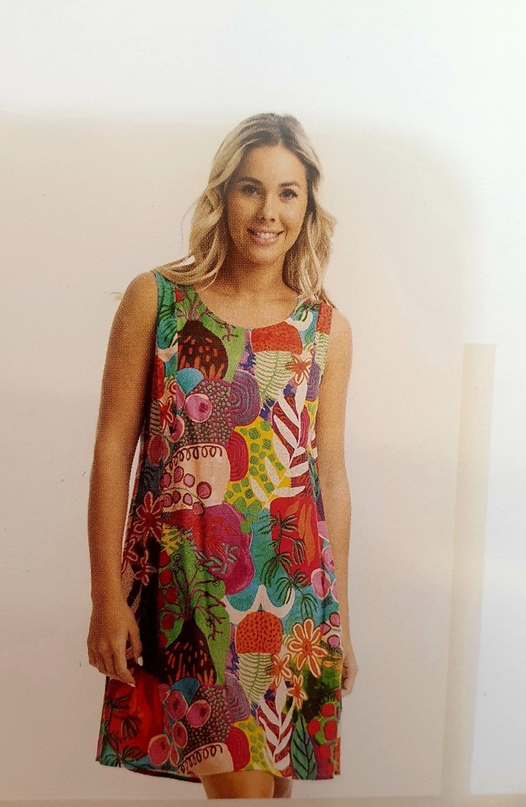 Woman smiling in a colorful, sleeveless dress with floral and striped patterns.