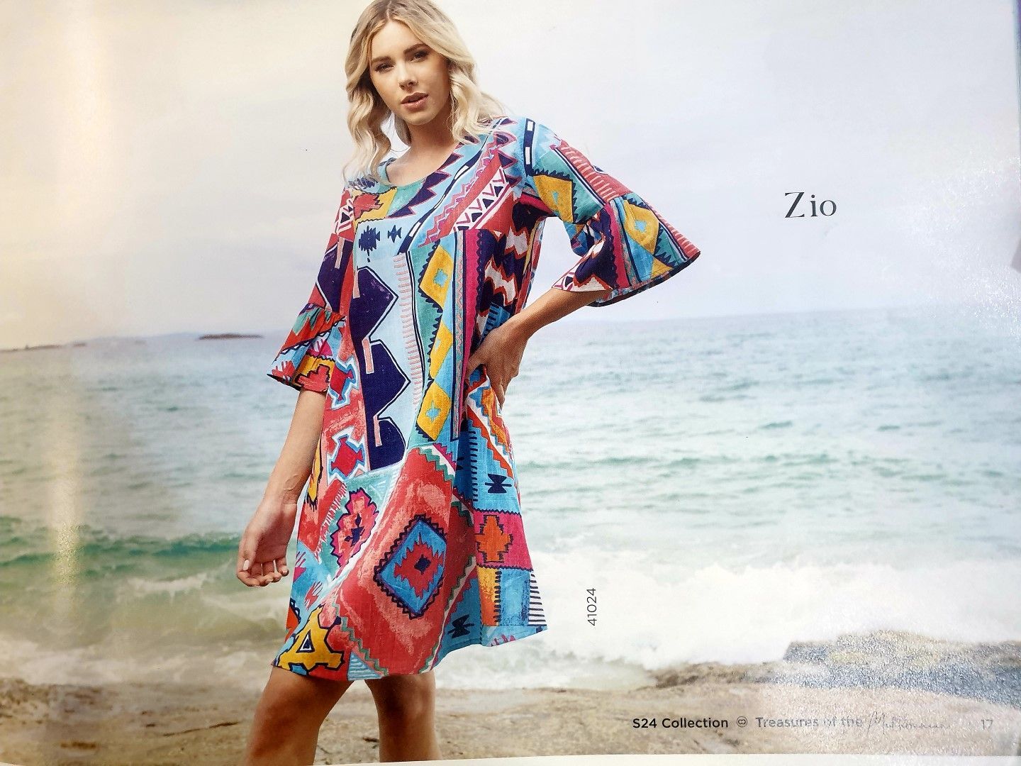 Woman in colorful patterned dress by the ocean.