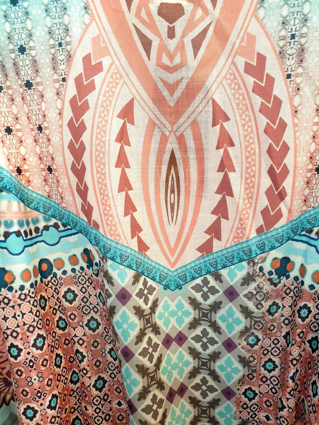 Close-up of a patterned top with geometric and tribal designs in teal, peach, and brown.