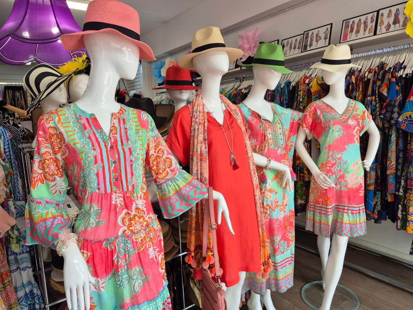 Mannequins wearing colorful dresses and hats in a retail store.
