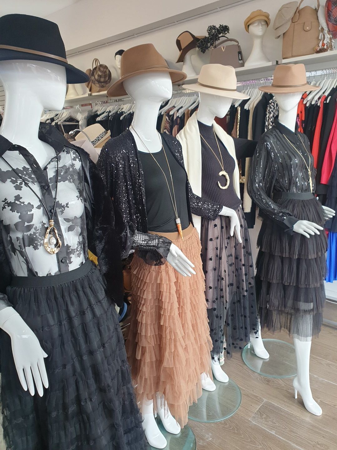 Mannequins in a clothing store, wearing hats, blouses, skirts, and accessories.