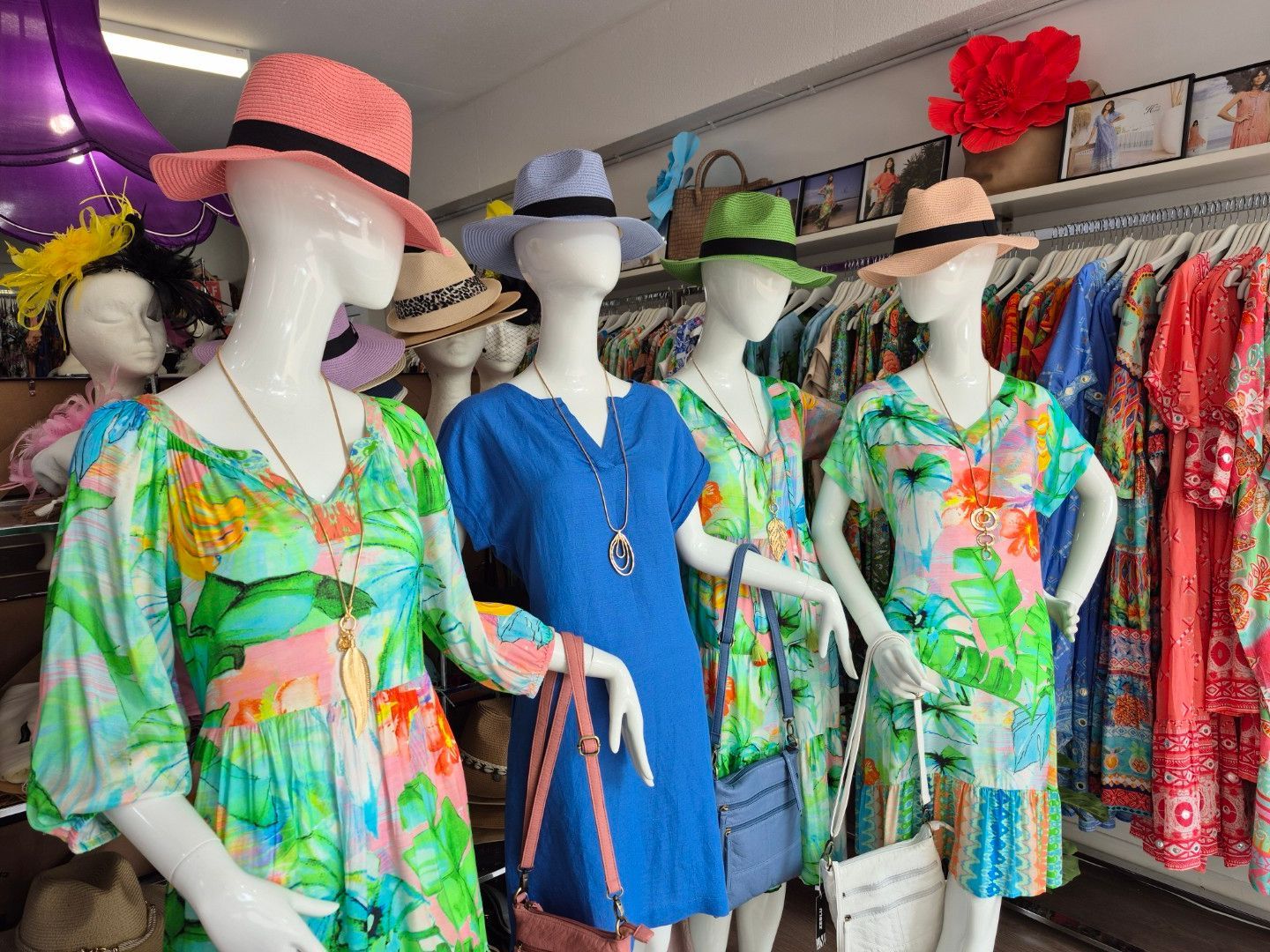 Mannequins wearing colorful dresses and hats in a clothing store.