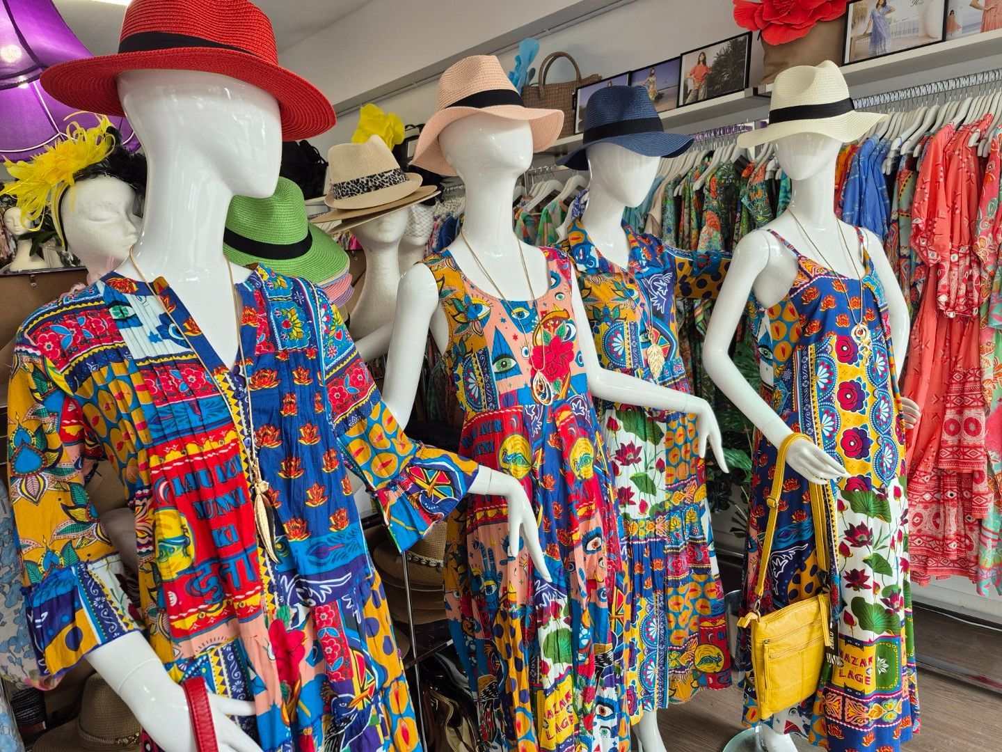 Mannequins wearing colorful patterned dresses and hats displayed in a boutique.