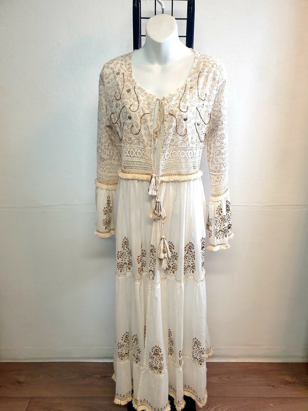 White dress with long sleeves, gold embroidery, on a mannequin.