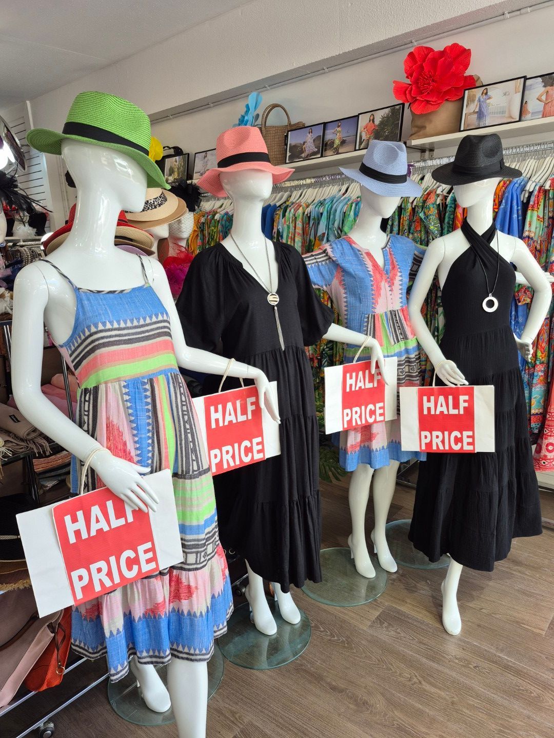 Mannequins in summer dresses, hats, holding half-price signs, inside a shop.