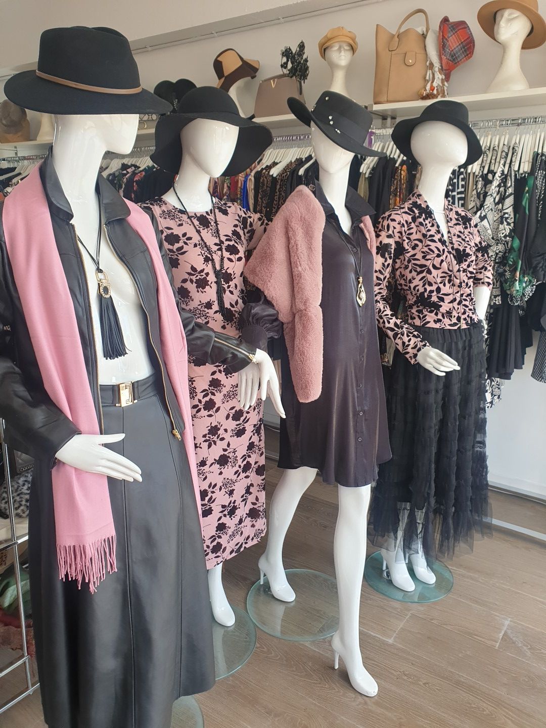 Mannequins in a clothing store display various outfits: coats, dresses, hats, and skirts.