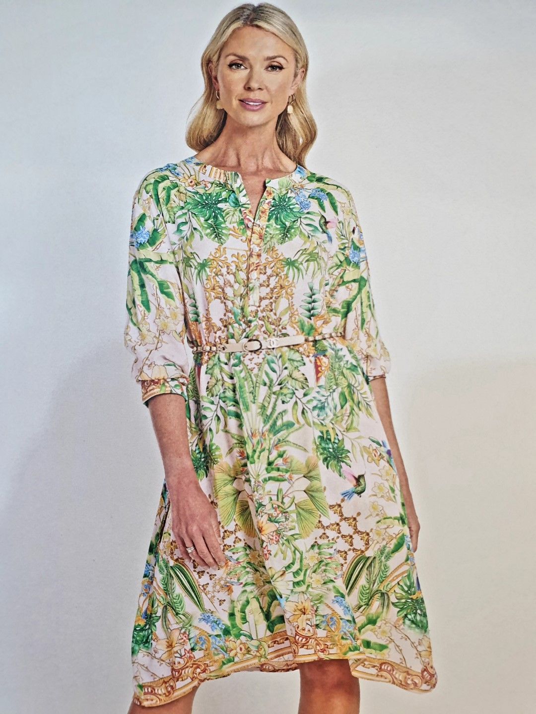 Woman in a floral print dress, belted at the waist, smiling.