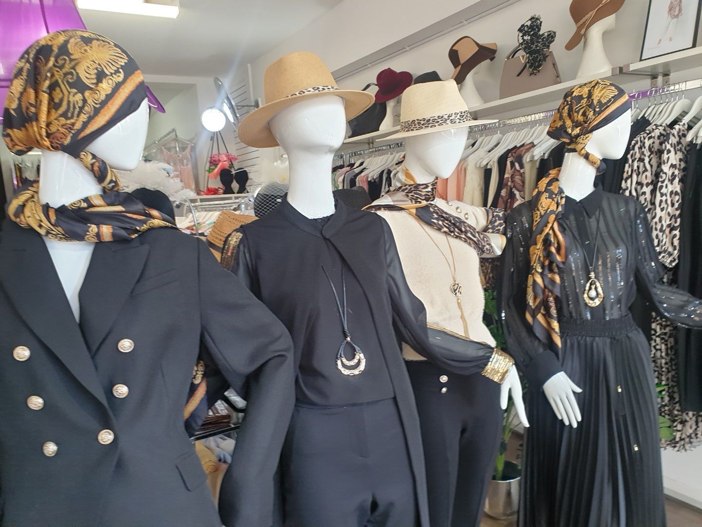 Mannequins in a clothing store displaying various outfits, including headscarves and hats, in black, gold, and beige.