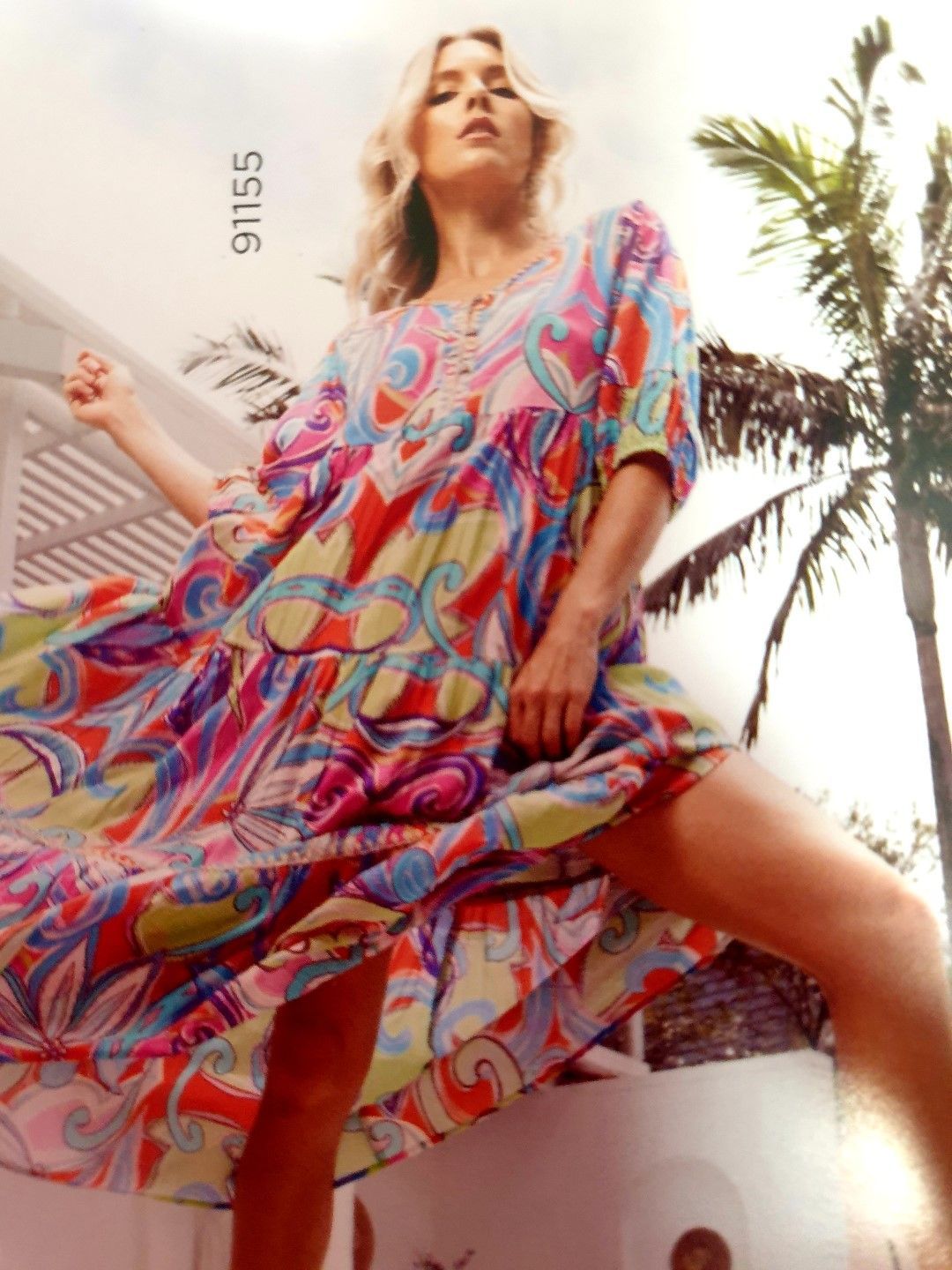 Woman in colorful patterned dress, outdoors near palm tree.
