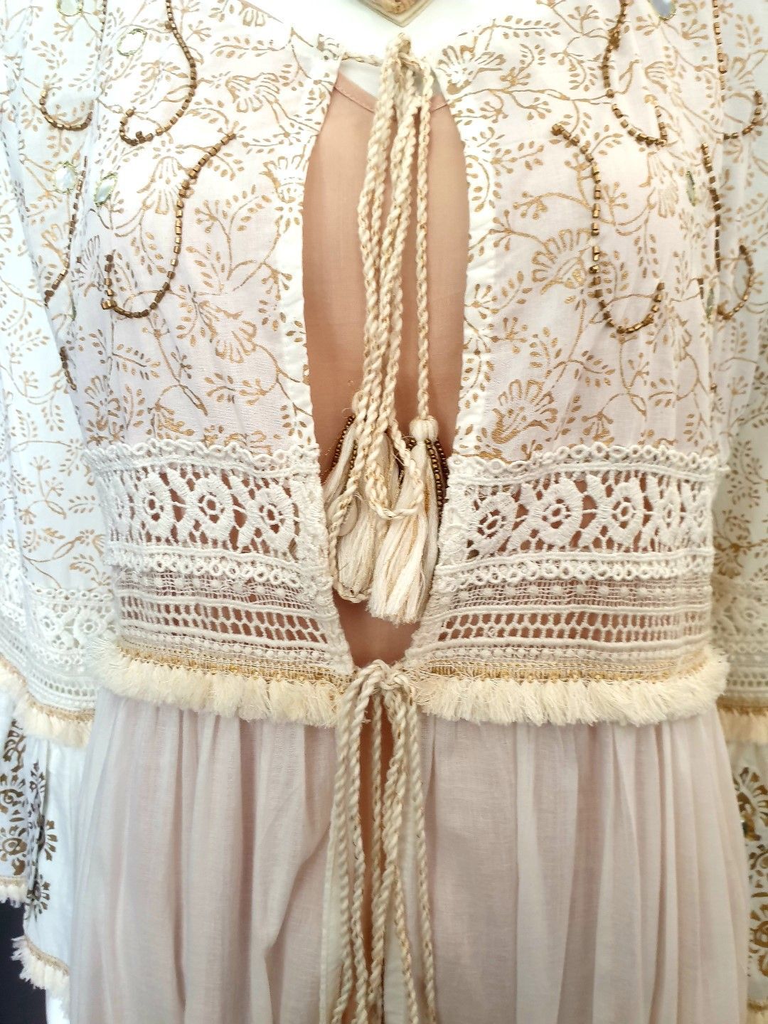 Cream-colored lace jacket with gold embroidery tied at the bust, over a light pink dress.