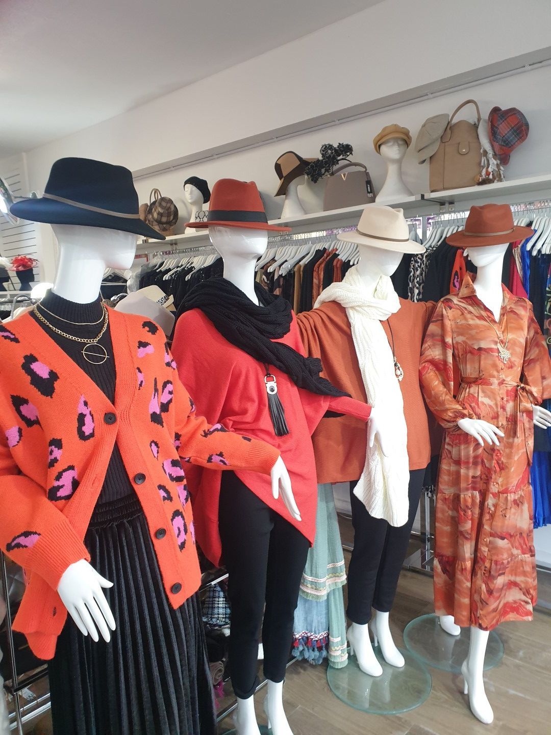 Four mannequins in a clothing store, wearing hats and outfits in shades of orange, black, and white.