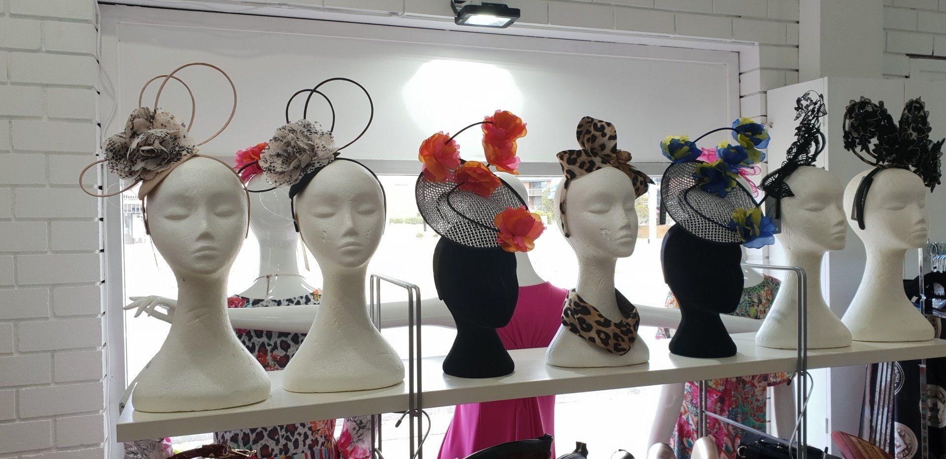 Mannequin heads displaying colorful headpieces on a shelf, set against a white brick wall.