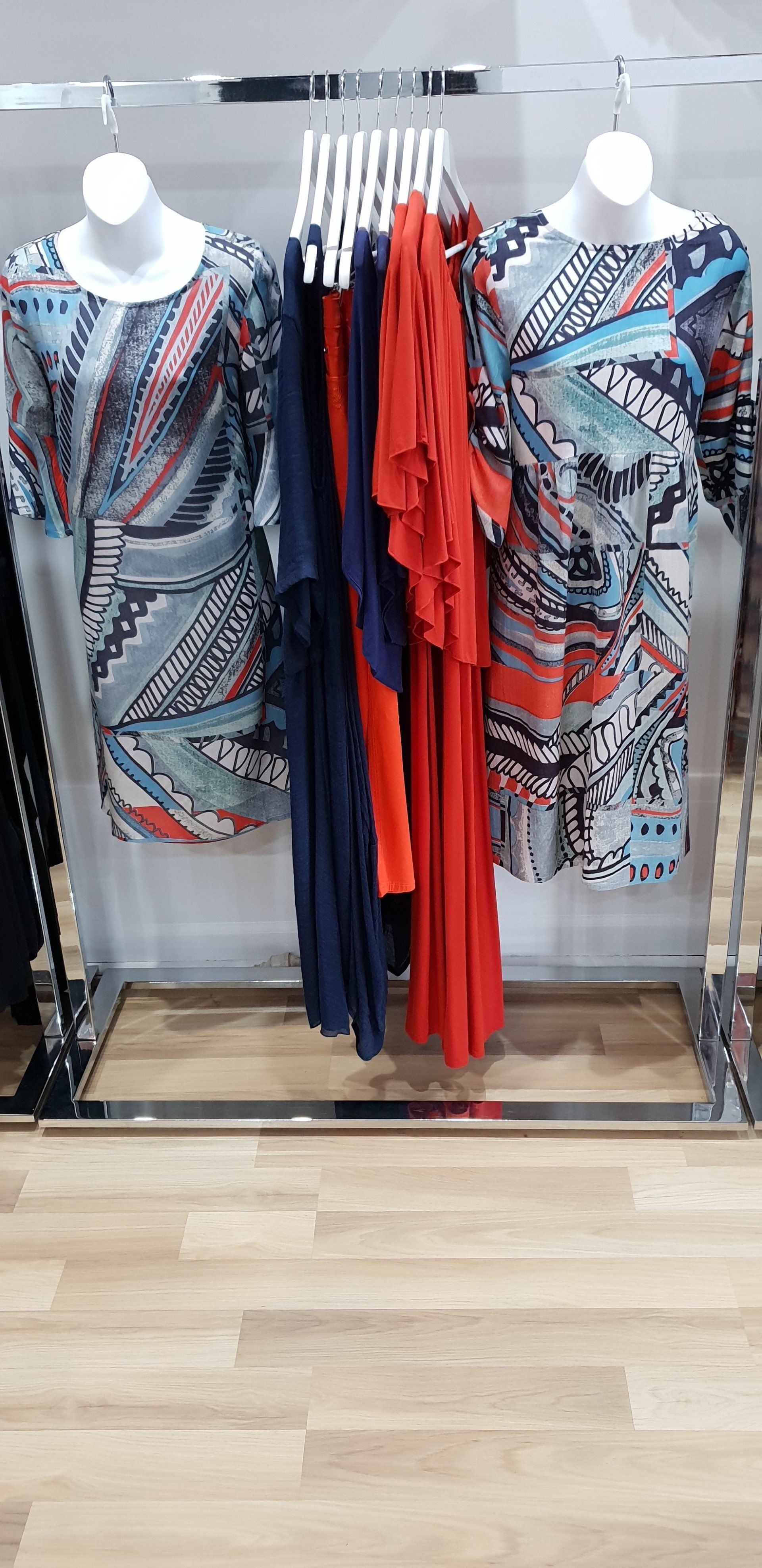 Clothing display in a retail store, featuring dresses on mannequins and hangers. Wooden floor.