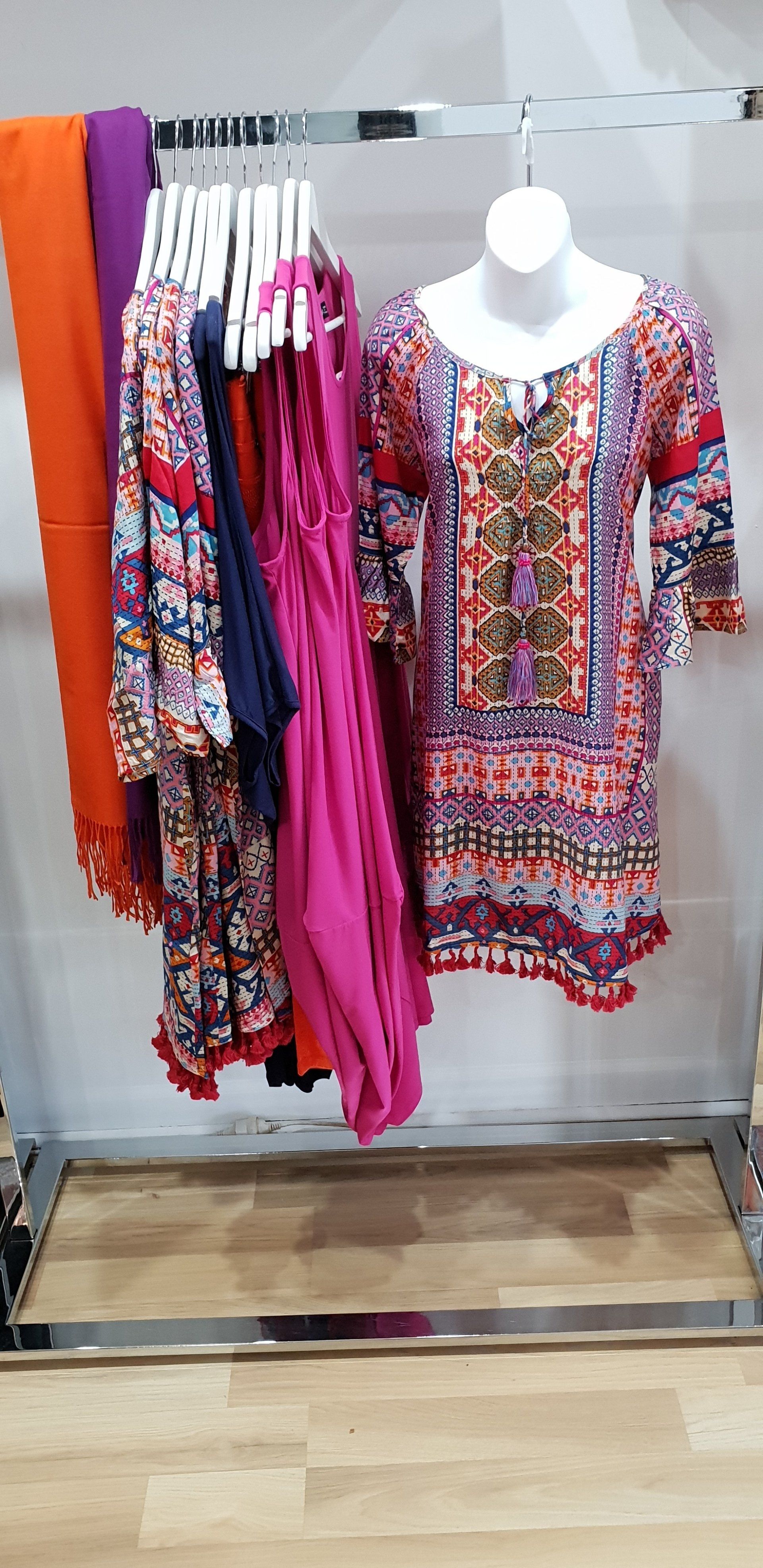 Clothing rack with dresses and scarves; a mannequin displays a printed dress.