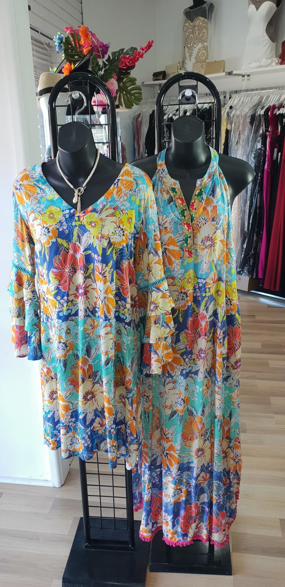 Two mannequins in a clothing store wearing floral print dresses.