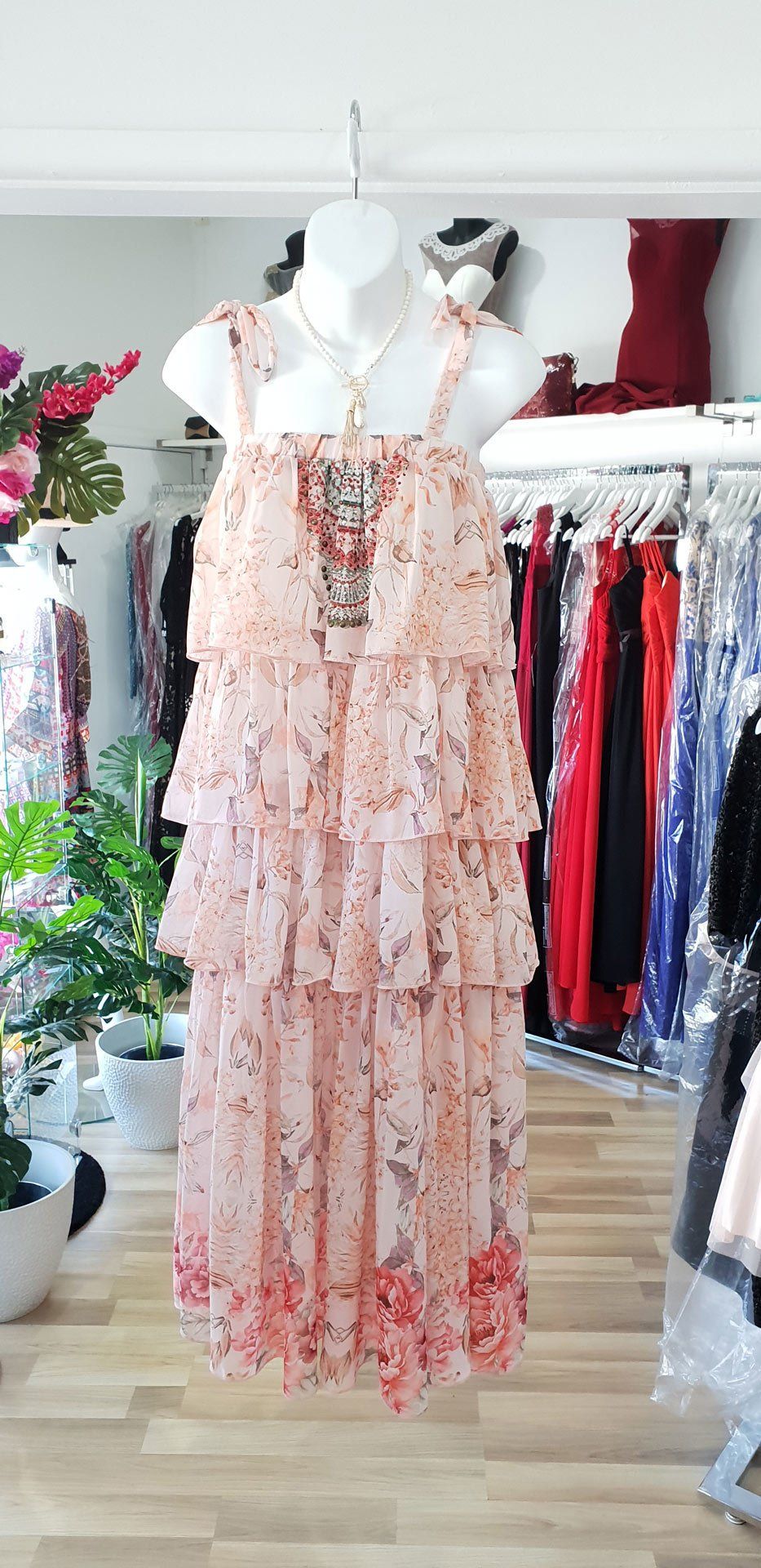 A floral, layered dress hangs on a mannequin in a clothing store.