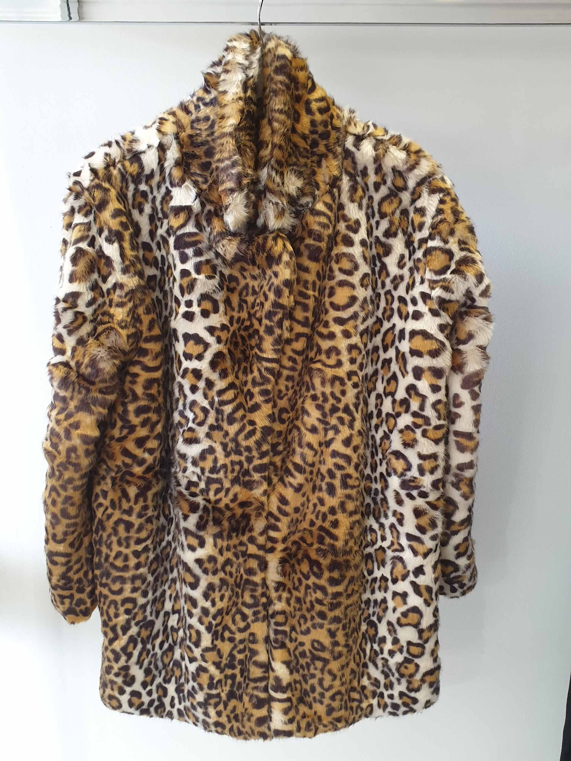 Leopard print faux fur coat hanging on a white hanger against a white wall.