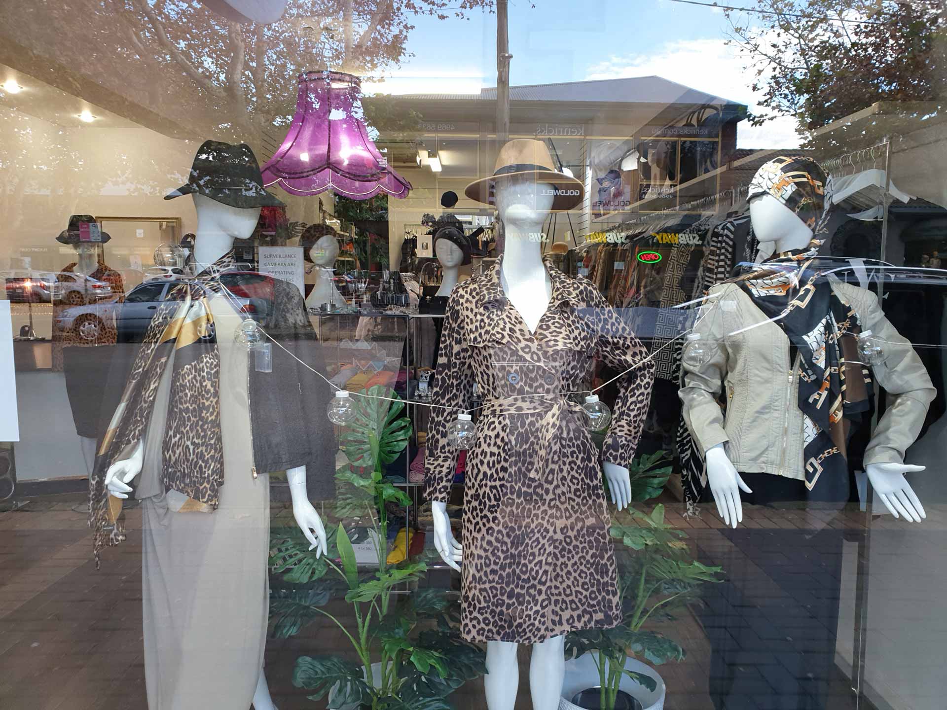 Window display with mannequins wearing leopard print dresses and hats, set inside a clothing store.