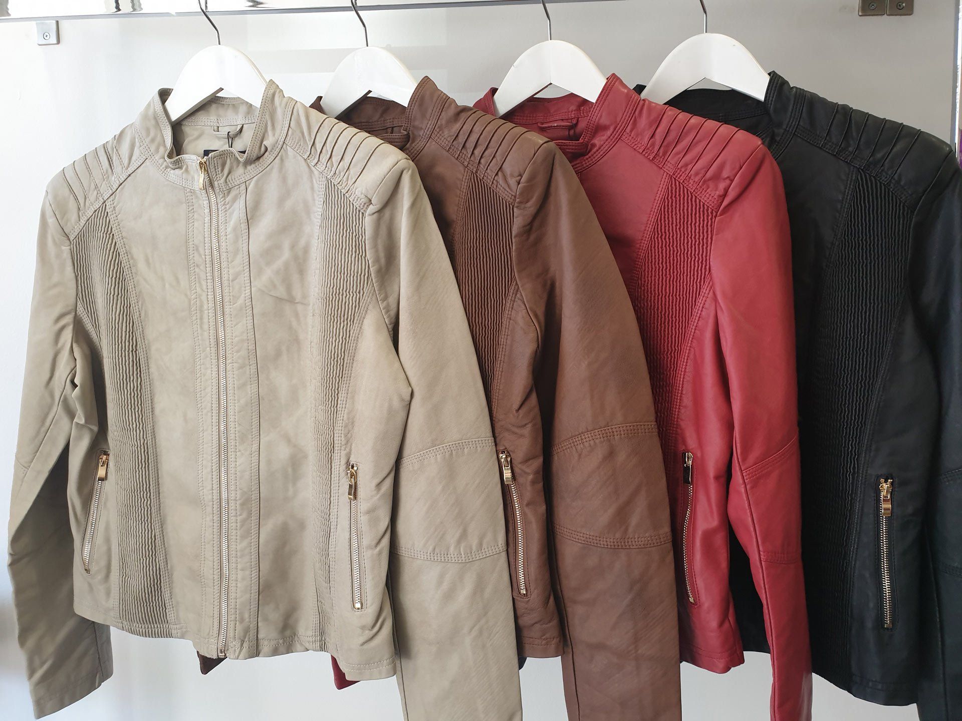 Four jackets in varying shades of brown and red hang on white hangers.