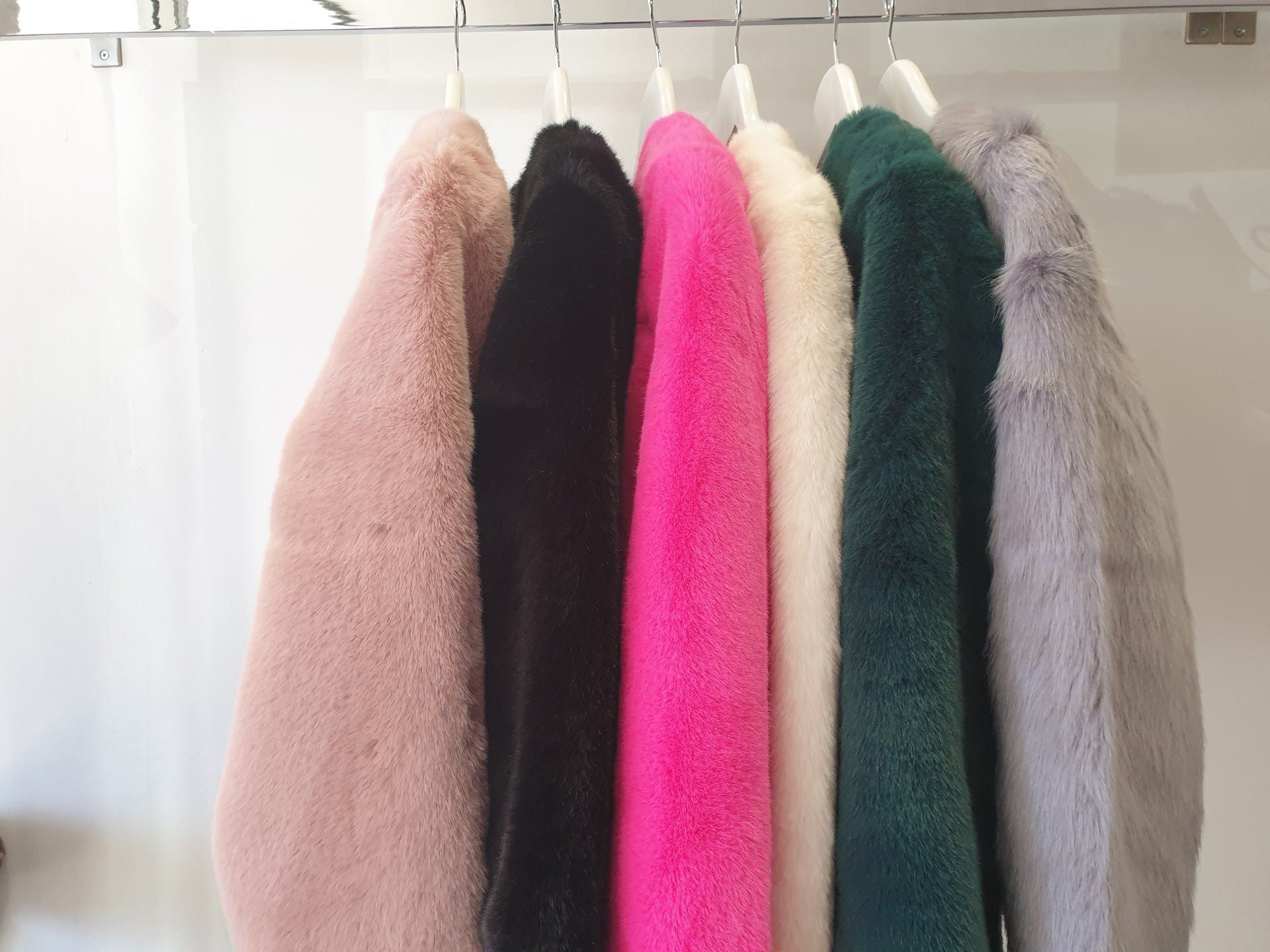 Coats in shades of pink, black, fuchsia, white, green, and gray hanging on a rack.