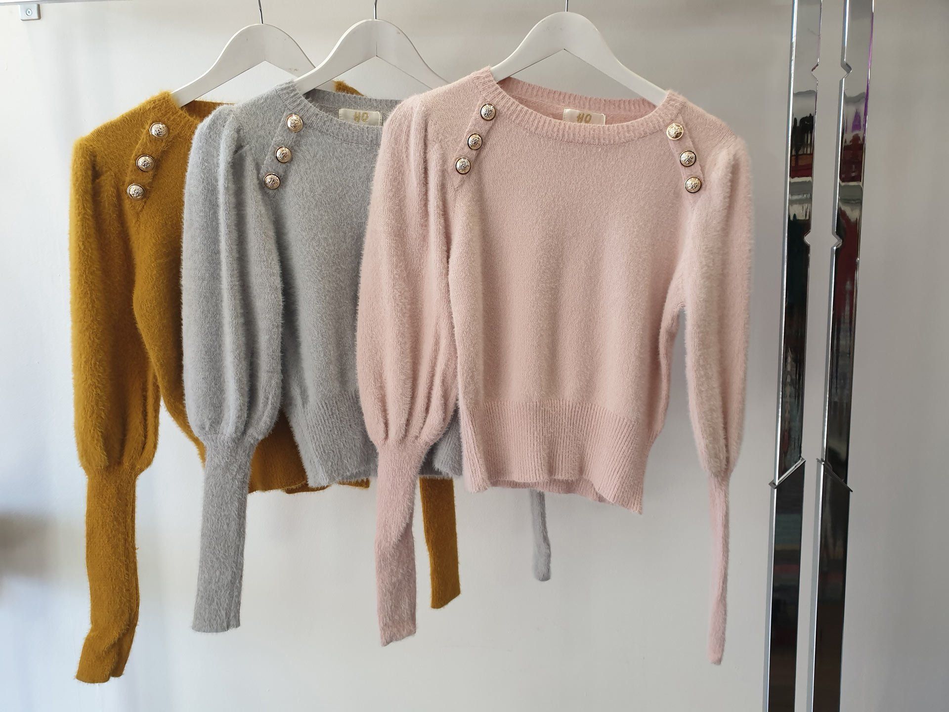 Three sweaters with button details on hangers: mustard, gray, and pink.