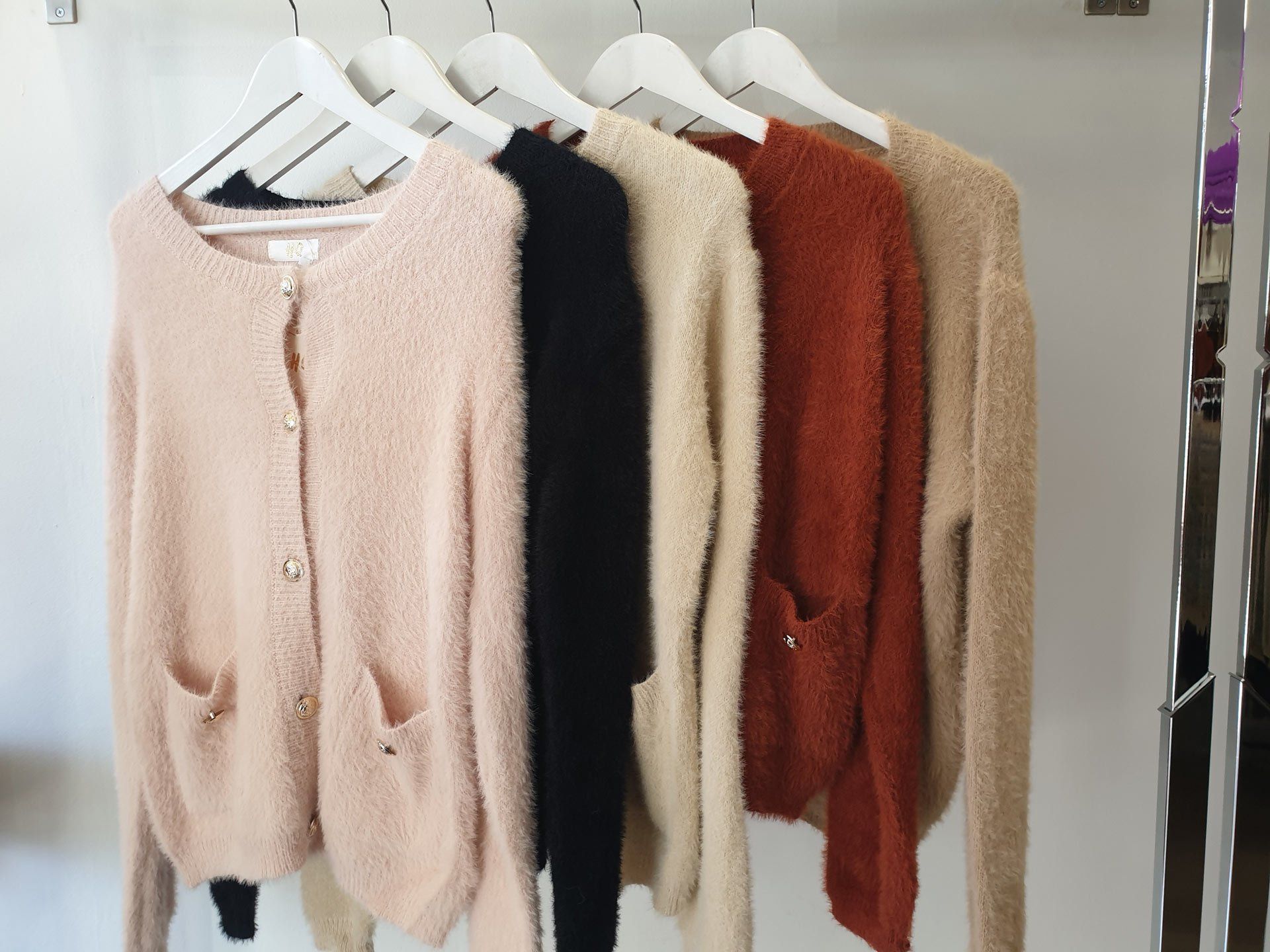 Row of fuzzy cardigans in peach, black, cream, burnt orange, and tan on white hangers.