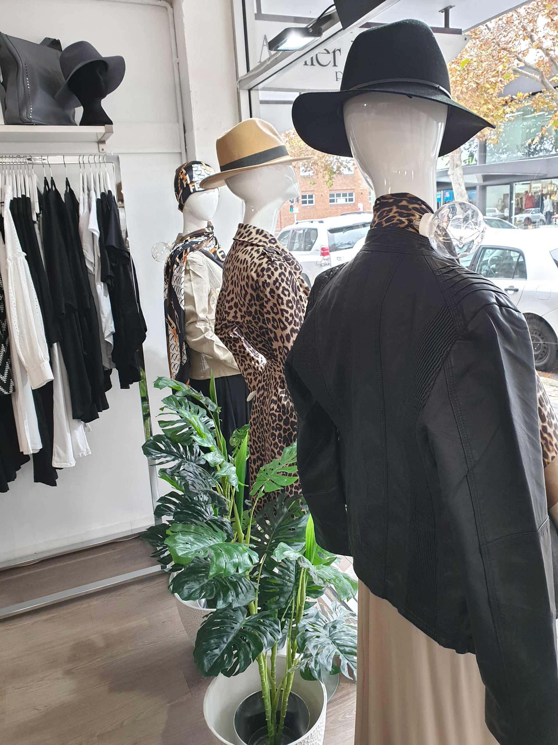Clothing store display with mannequins wearing hats and jackets. Shelves hold black and white clothing.