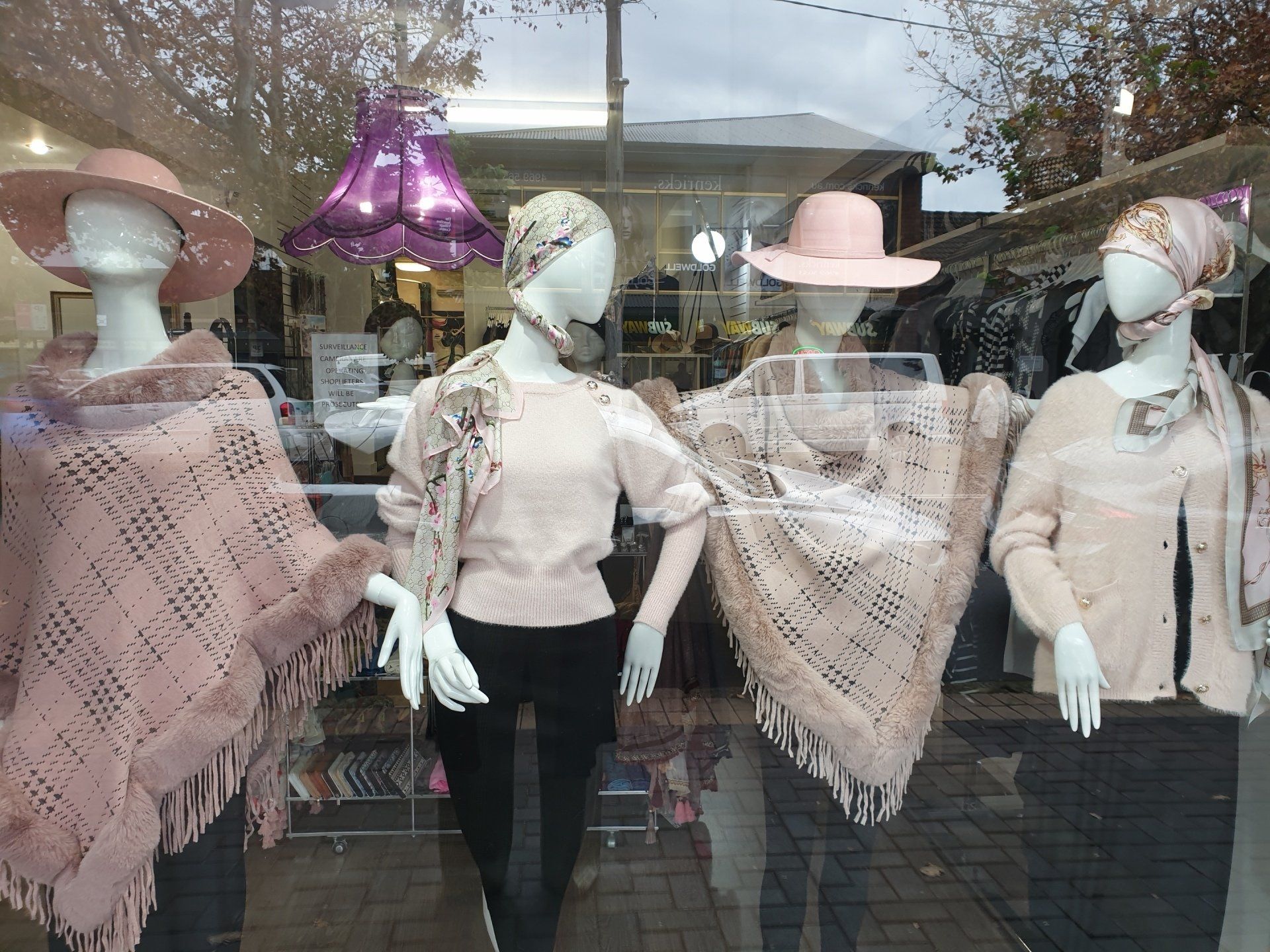 Window display of mannequins in pink clothing, hats, and shawls.