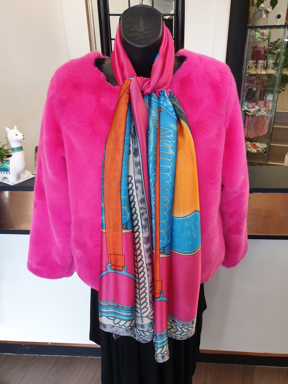 Hot pink faux fur jacket with a printed scarf tied on a mannequin.