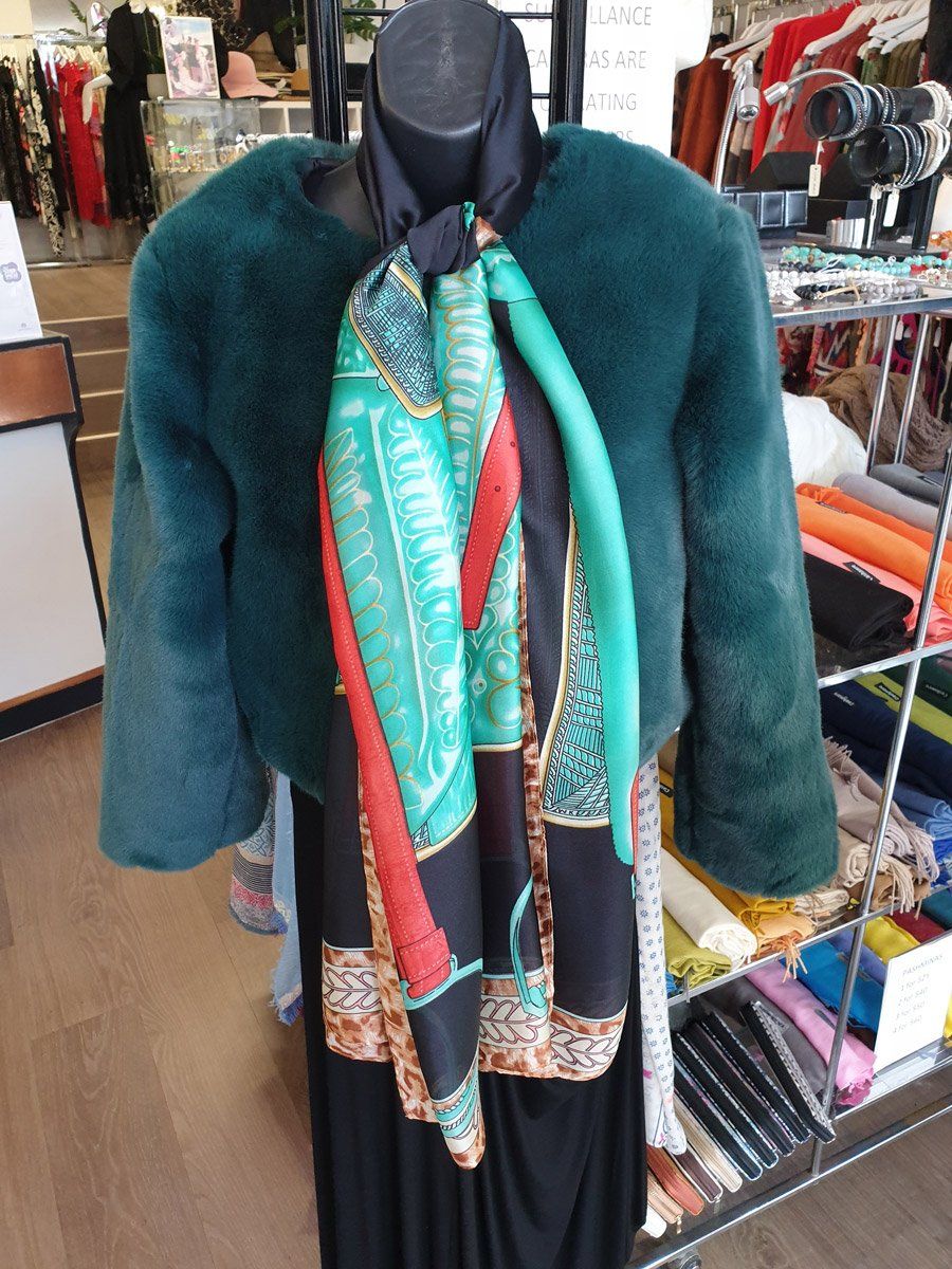 Mannequin in a shop: emerald fur jacket over a dress, with a patterned scarf.
