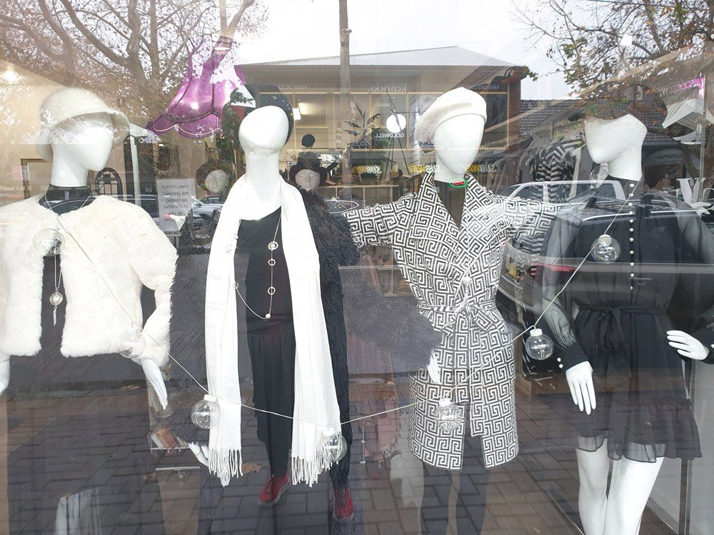 Window display of mannequins in various outfits, featuring hats, scarves, and dresses.