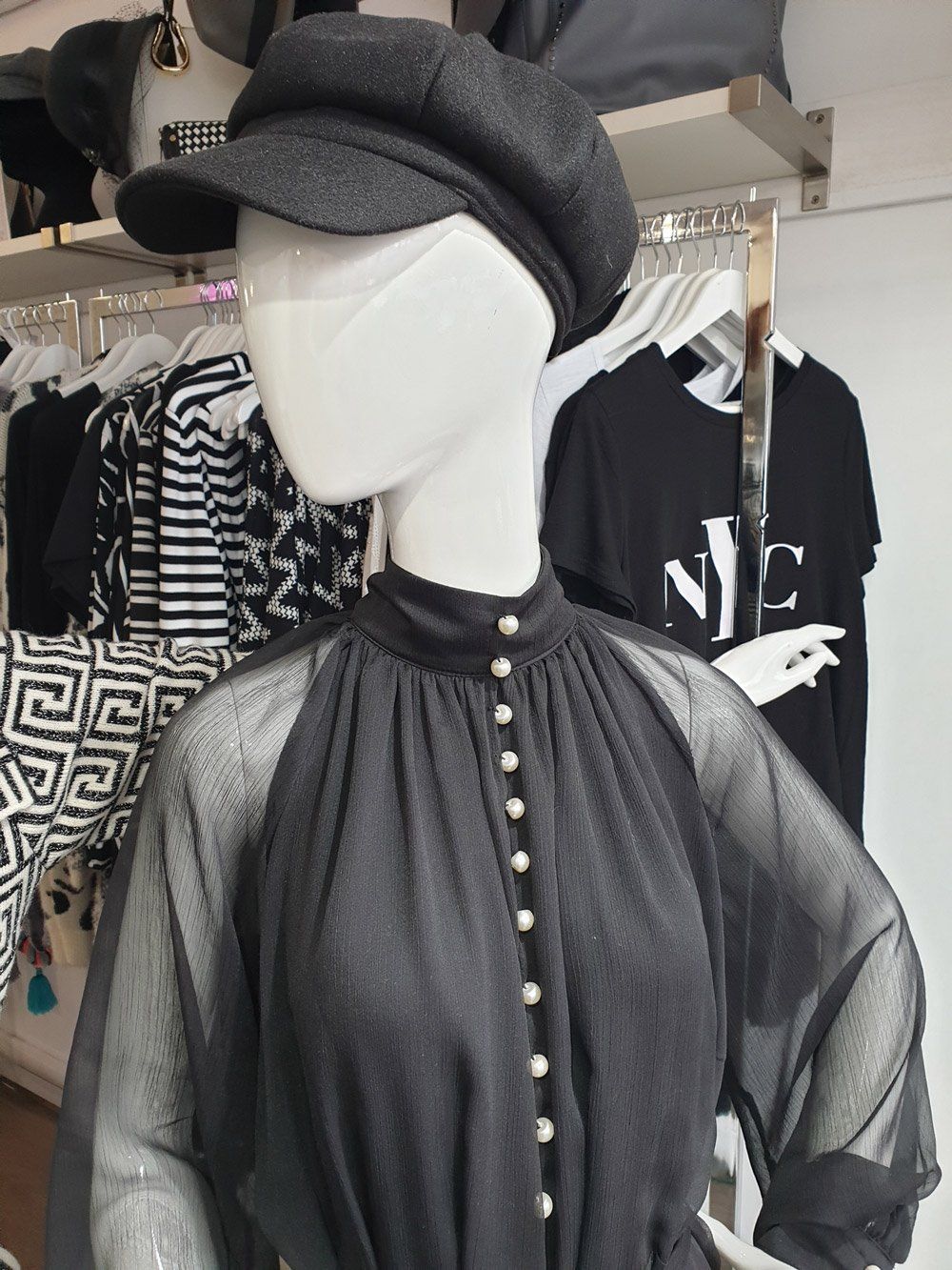 Mannequin in black dress and hat, posing in a clothing store.