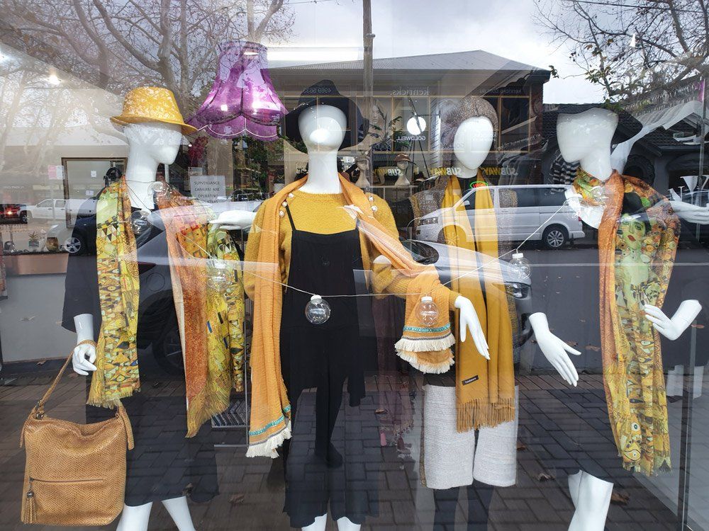 Four mannequins in a shop window wearing outfits in yellow, black, and white. The street and reflections are visible.