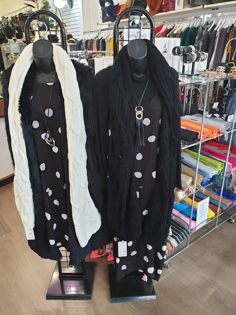 Two mannequins in a clothing store wearing polka dot dresses, scarves, and necklaces.