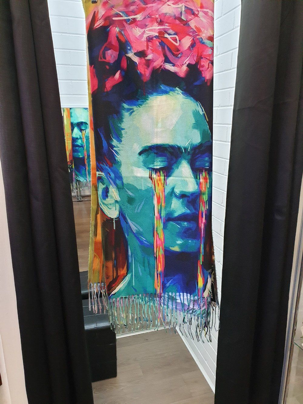 Frida Kahlo art tapestry with colorful tears hanging in a room, framed by black curtains.