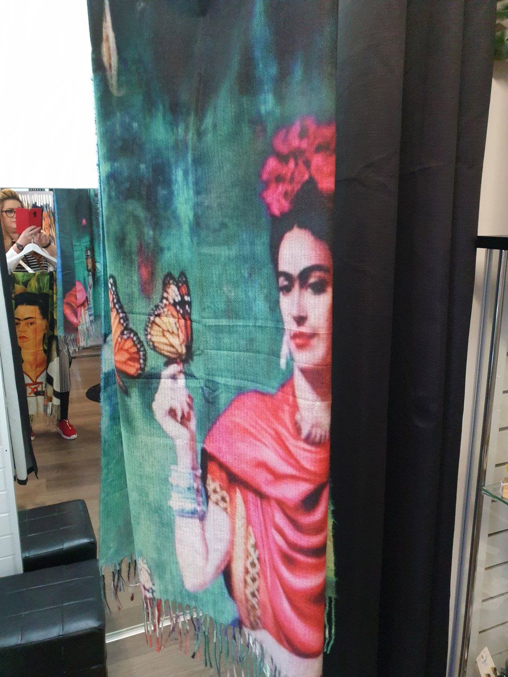 Frida Kahlo scarf with butterfly in a store. Bright colors, red shawl, floral headpiece, green background.