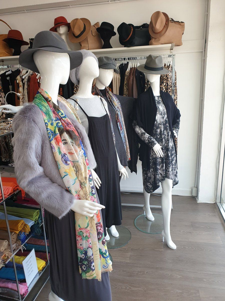 Mannequins wearing clothes and hats in a boutique, with hats displayed on a shelf.