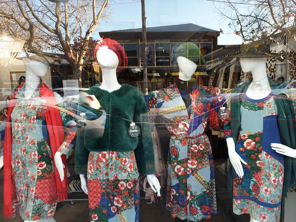 Four mannequins in a shop window display colorful floral and patterned outfits.