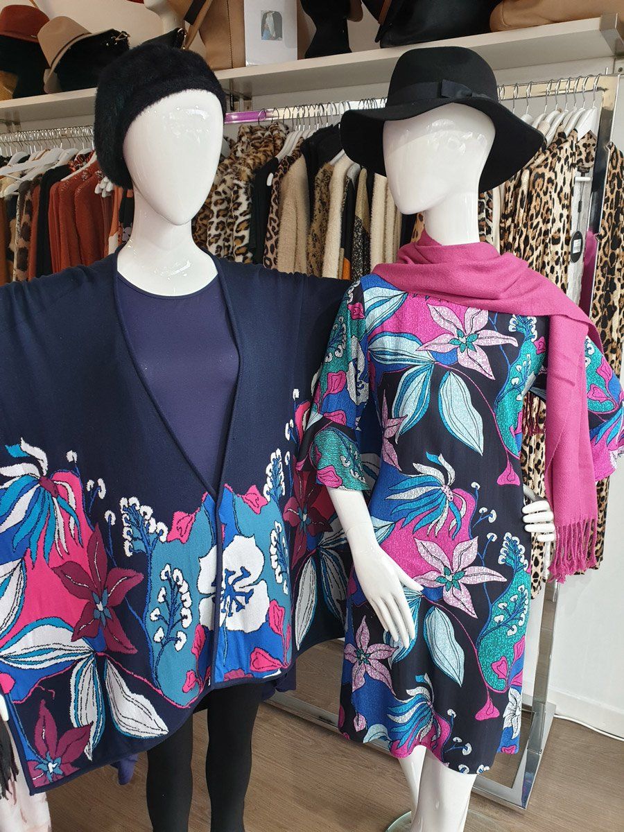 Two mannequins in a clothing store. One wears a floral cape, the other a floral dress and pink scarf.