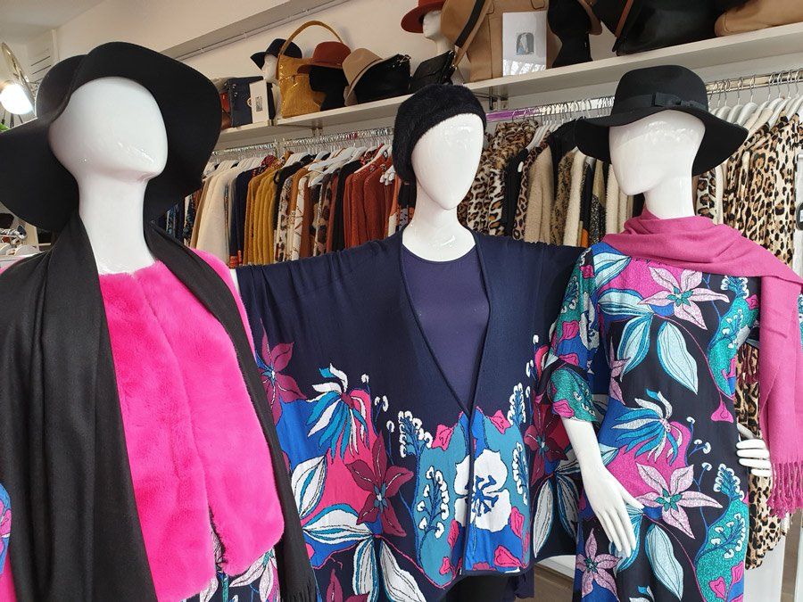 Three mannequins in a clothing store display floral dresses, hats, and scarves.