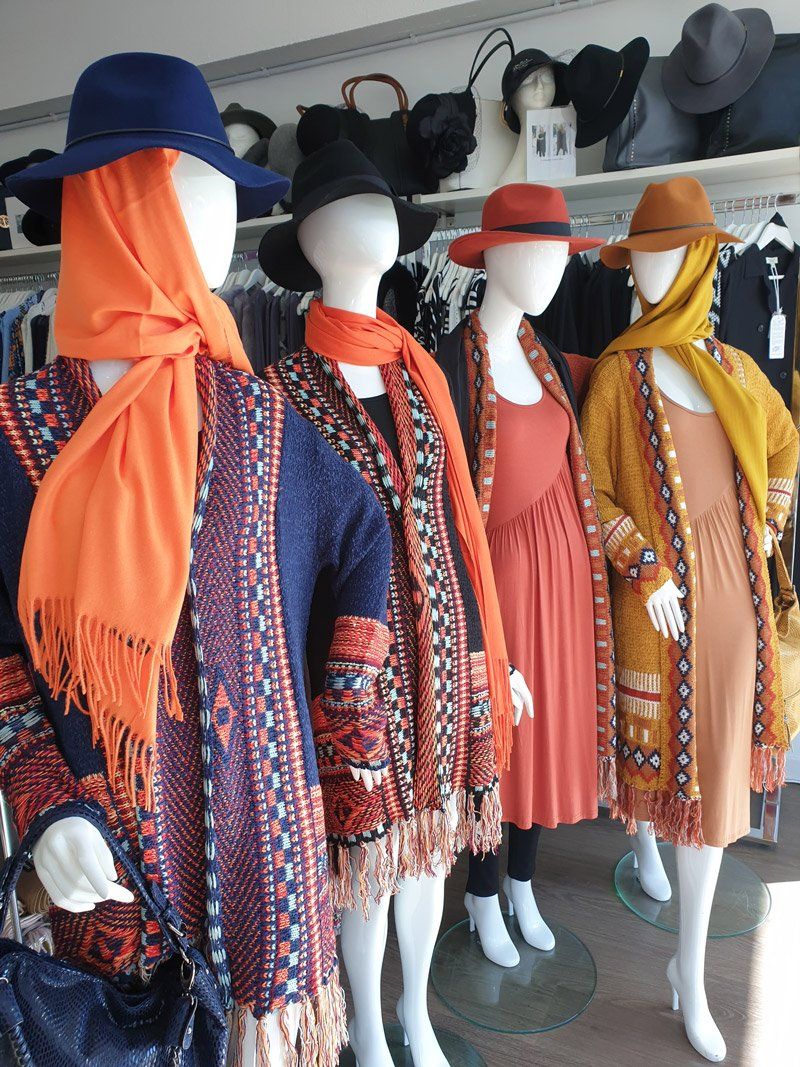 Four mannequins in a shop window, wearing hats, scarves, and colorful patterned clothing.