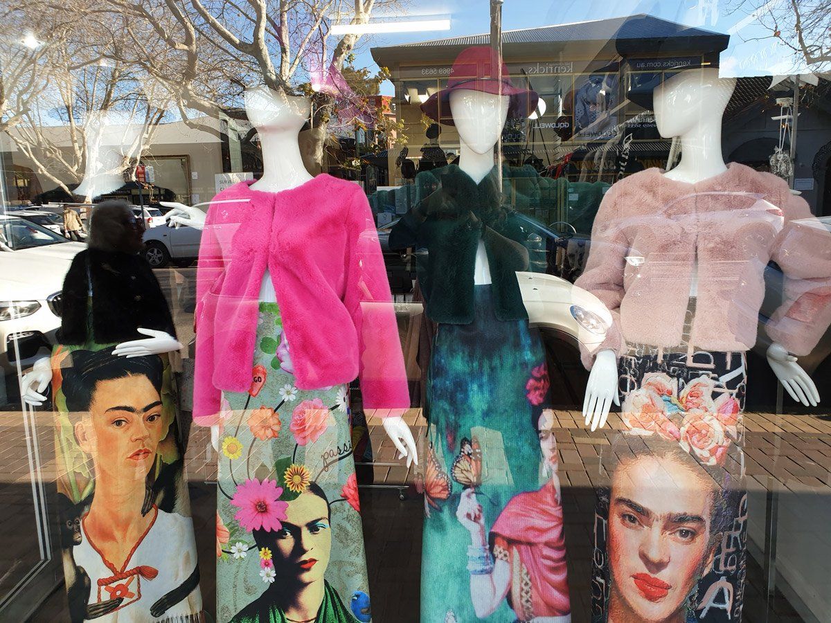 Window display with mannequins wearing colorful outfits featuring Frida Kahlo art.