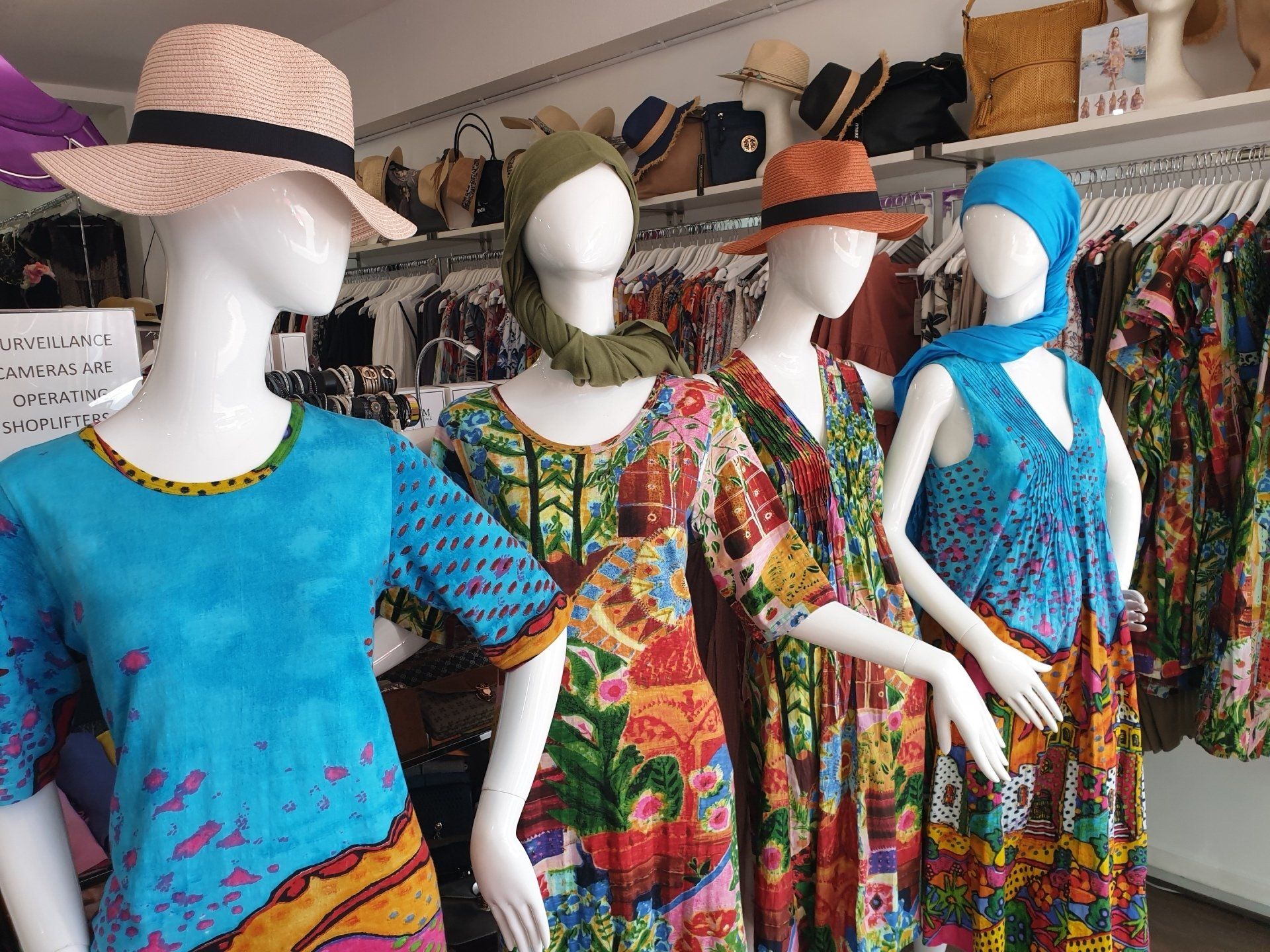 Four mannequins wearing colorful dresses and hats in a clothing store.