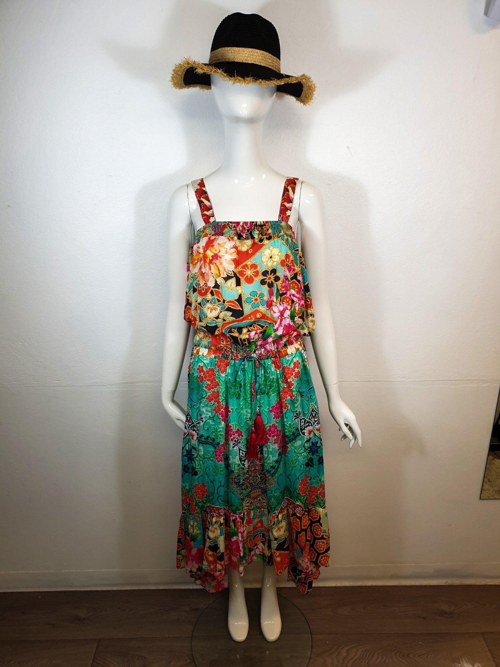 Mannequin in a colorful floral print dress and a black straw hat in a bright white room.
