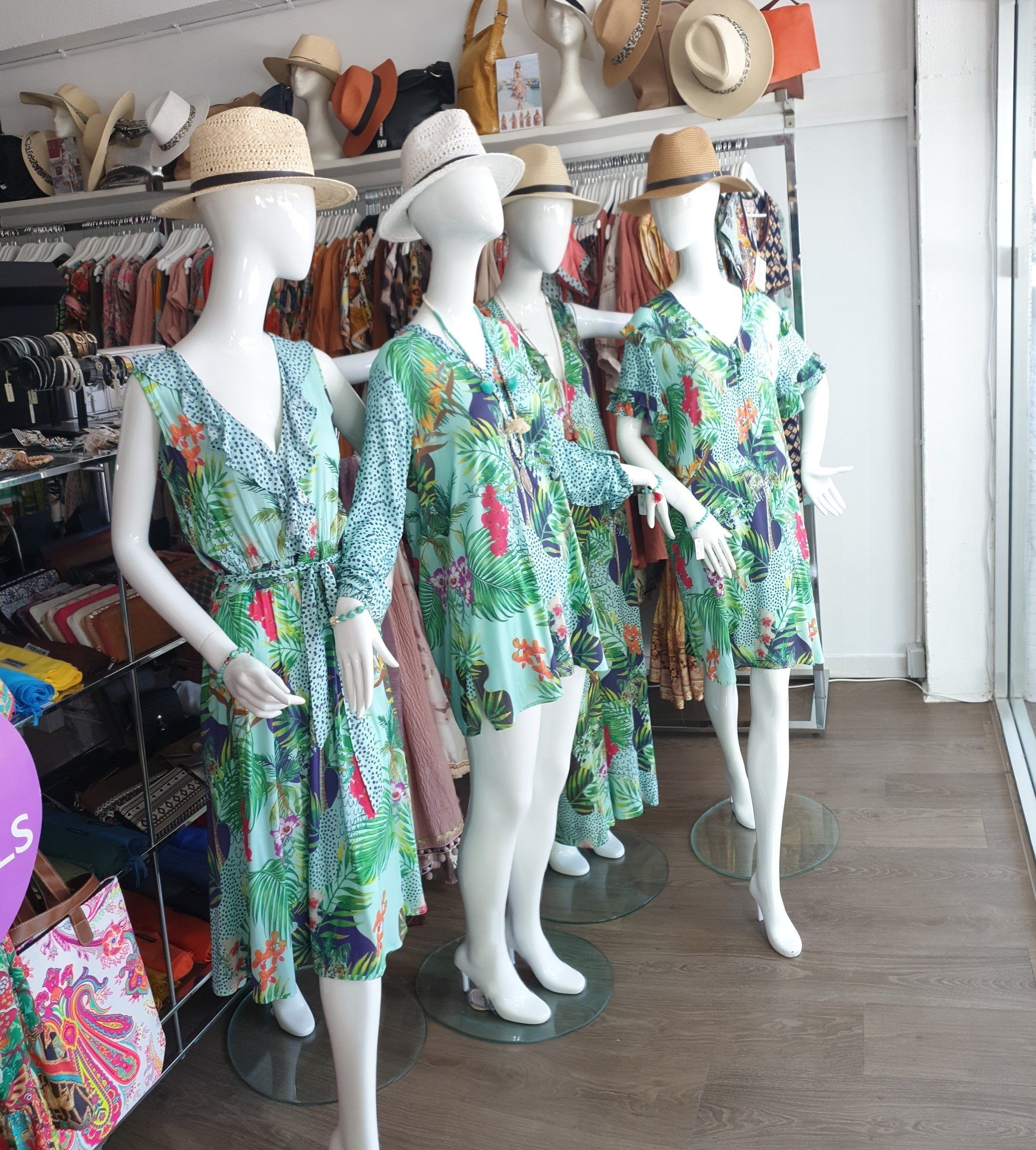 Four mannequins wearing floral dresses and hats in a store.