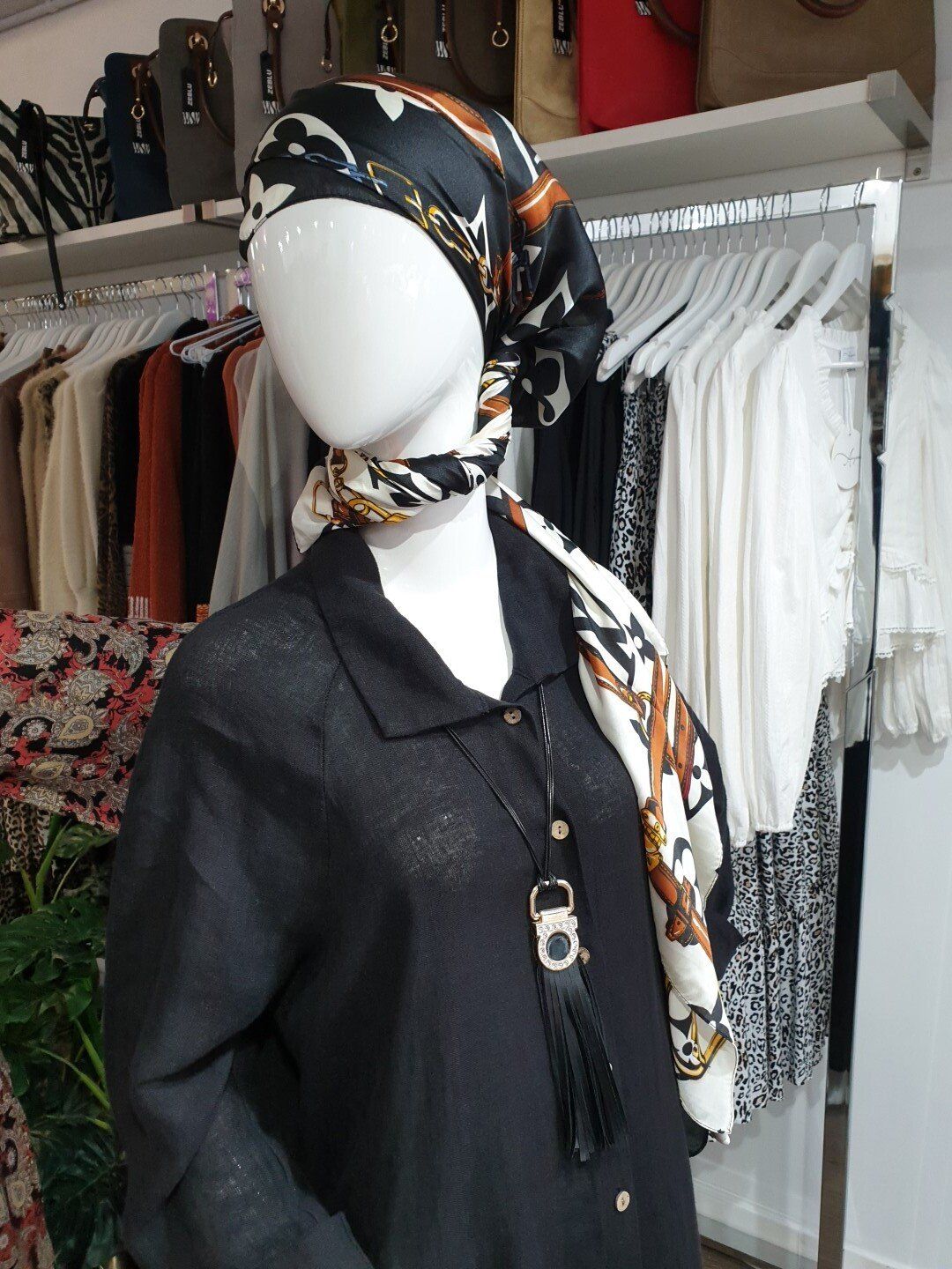 Mannequin in black shirt and scarf, wearing a printed headscarf, in a clothing store.