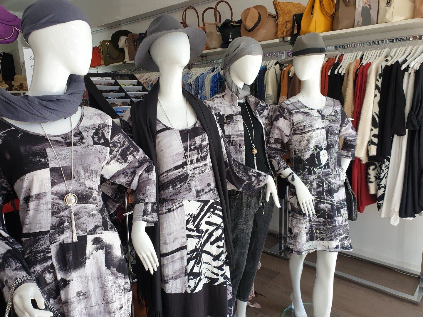 Four mannequins wearing black and white print dresses and hats in a clothing store.