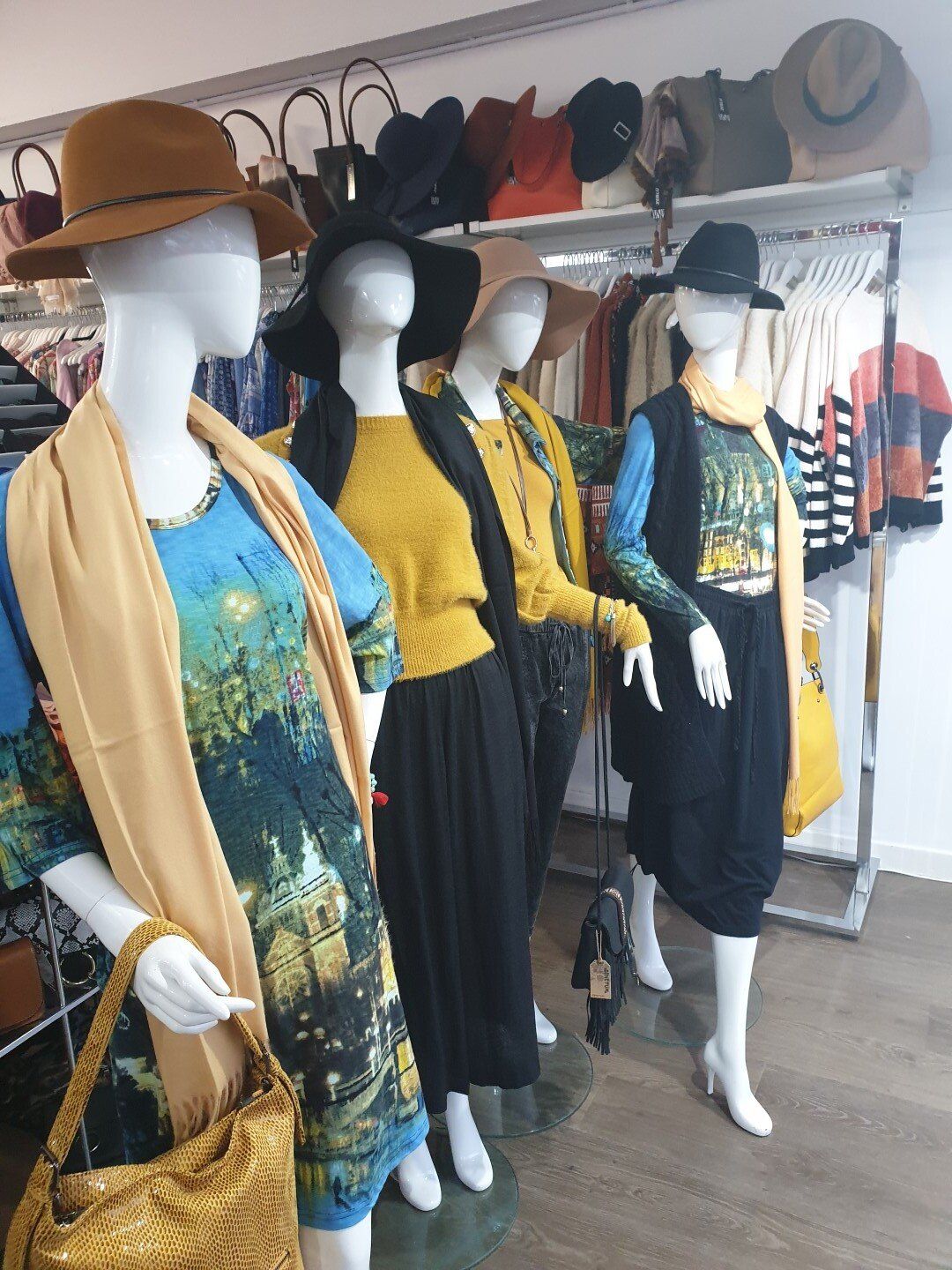 Mannequins wearing stylish outfits in a clothing store, featuring hats, scarves, and various colors.