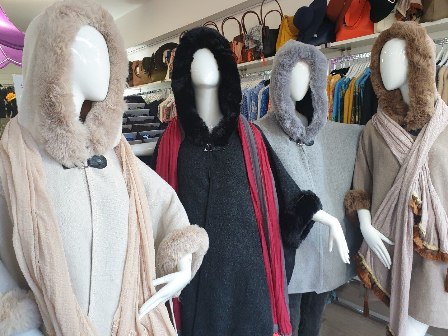 Four mannequins wearing hooded capes in a shop, beige, black, gray, and brown.